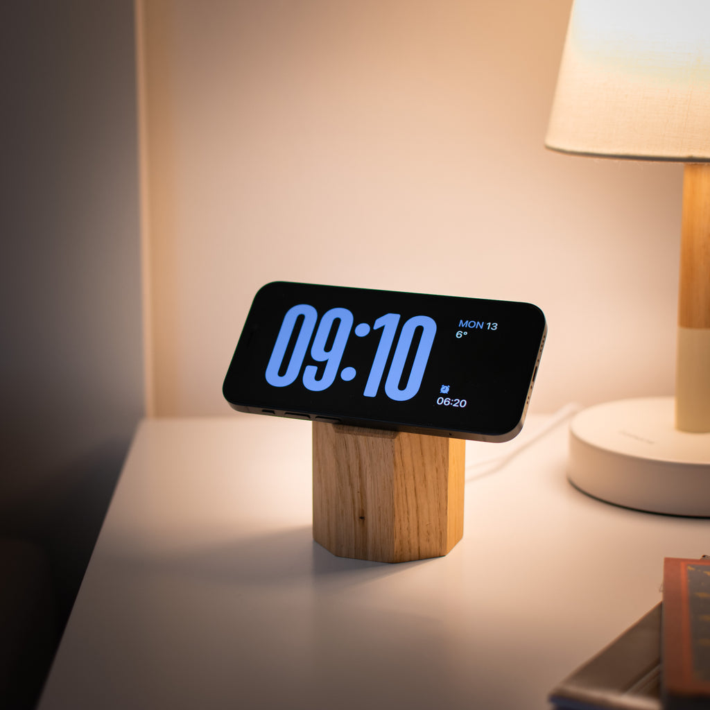 Digital clock with wooden base on a nightstand next to a lamp